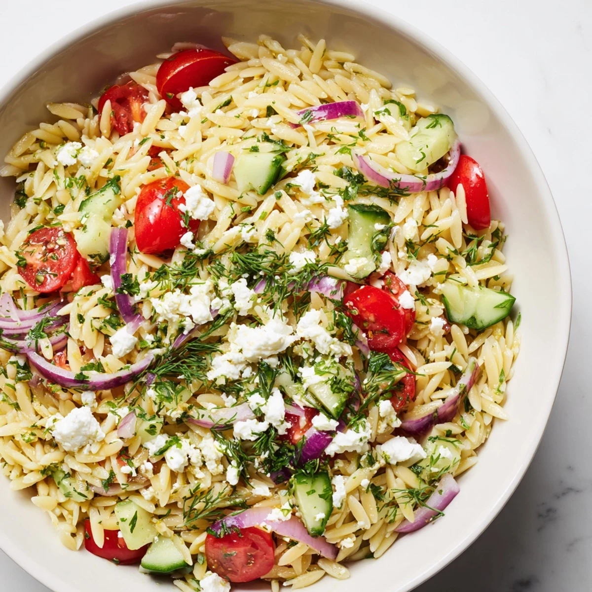 A close-up of Greek Orzo Salad with orzo, tomatoes, cucumber, feta, and olives in a serving bowl.