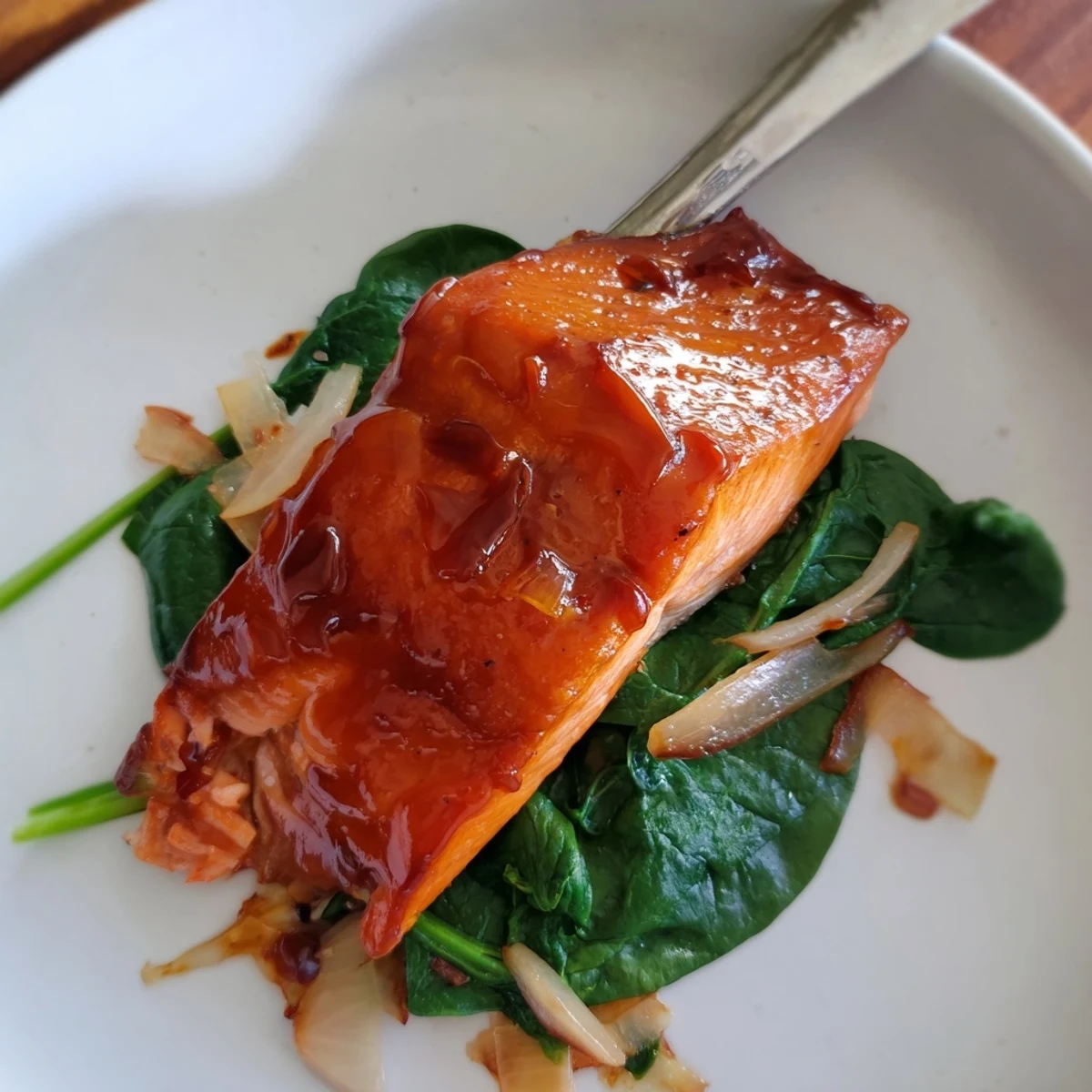 Golden miso salmon sits atop fresh sautéed spinach, garnished with lemon wedges for a bright, nutritious serving.