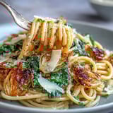 A close-up shows a hearty Cabbage Pasta With Garlic and Parmesan plated with lemon zest and extra Parmesan next to a glass of white wine.