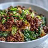 A hearty bowl of Chinese Ground Beef and Cabbage Stir-Fry served over steamed cauliflower rice, garnished with fresh green onions. 