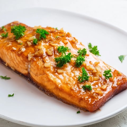 Golden-brown Honey Garlic Glazed Salmon fillets glistening with a buttery glaze, garnished with fresh parsley and lemon wedges on a rustic plate.