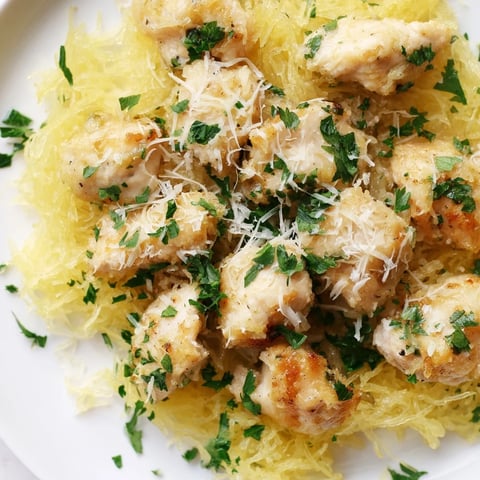 Tender lemon garlic chicken is spooned over roasted spaghetti squash strands, topped with grated Parmesan and fresh parsley for a light yet satisfying meal.