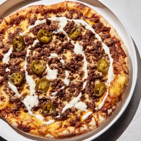 Mouthwatering Ground Beef Taco Pizza ready to slice, with a creamy sour cream drizzle and jalapeños.
