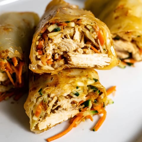 Freshly pan-fried Garlicky Pulled Chicken Wraps stuffed with tender shredded chicken, crisp lettuce, carrots, and cucumbers on a white plate.  