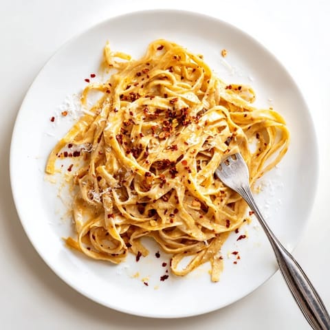 This Sriracha Honey Pasta features tender spaghetti strands swirled in a spicy-sweet garlic butter sauce, served in a rustic white bowl.