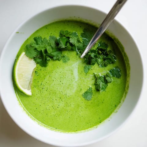 Creamy green Spinach Coriander Lemongrass Soup in a white bowl, garnished with fresh cilantro and lime wedges.