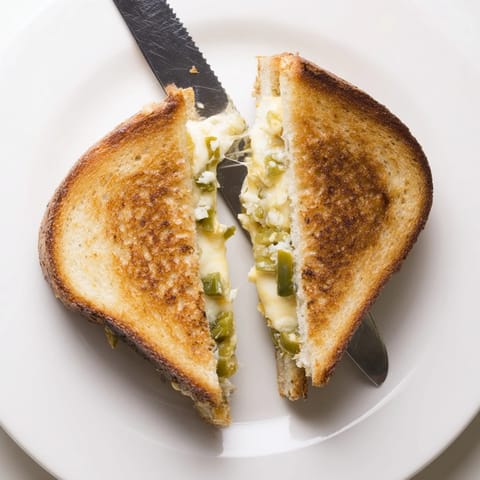 In a skillet, the jalapeño pepper jack grilled cheese sizzles, revealing creamy pepper jack and tangy pickled jalapeños.