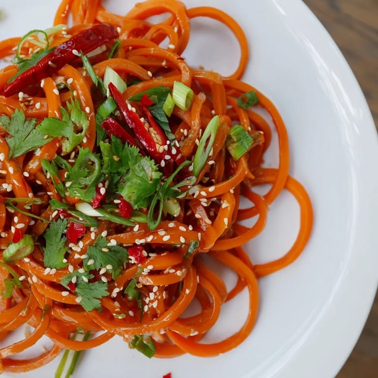 Freshly tossed Asian-style carrot ribbon salad with glossy sesame dressing, sliced green onions, and crunchy toasted seeds for a vibrant side dish.
