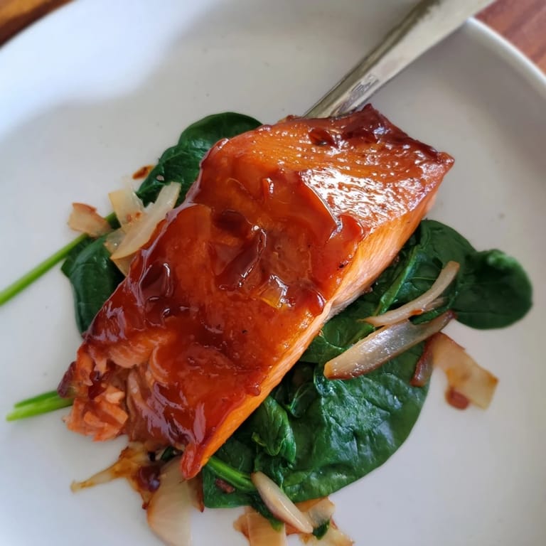Golden miso salmon sits atop fresh sautéed spinach, garnished with lemon wedges for a bright, nutritious serving.
