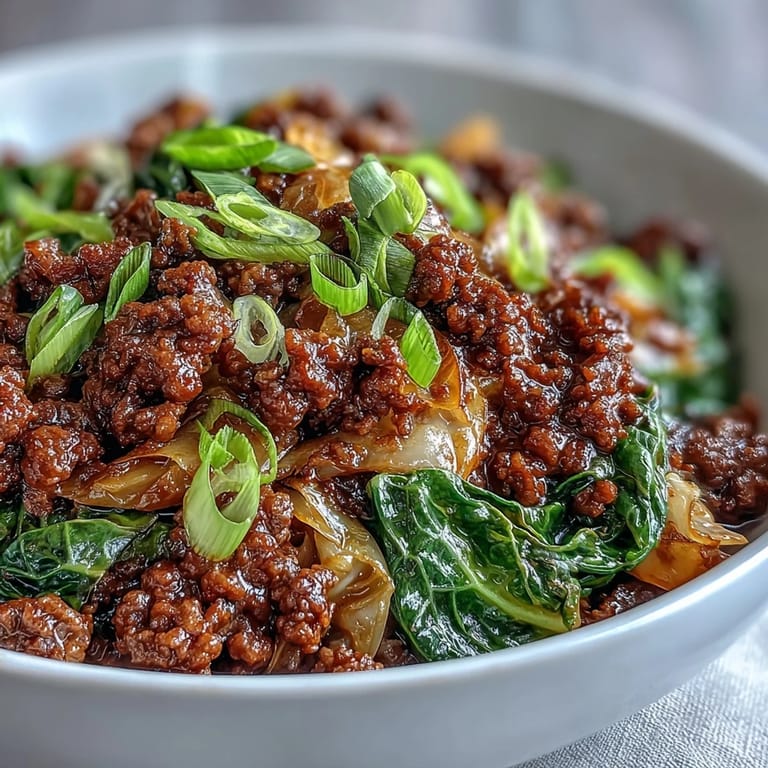 A hearty bowl of Chinese Ground Beef and Cabbage Stir-Fry served over steamed cauliflower rice, garnished with fresh green onions. 